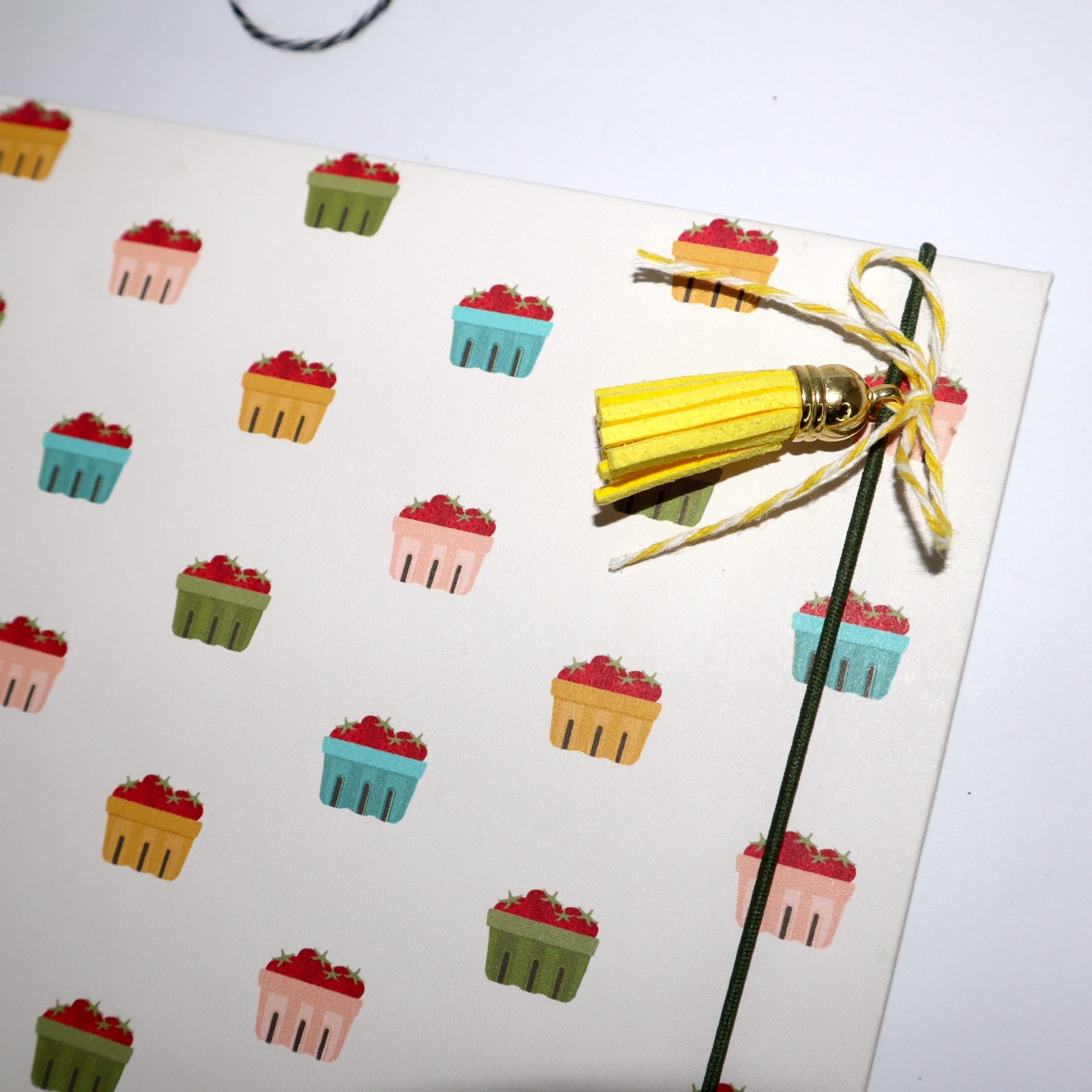 Capa de caderno com padrão de cestas coloridas e tassel amarelo no elástico