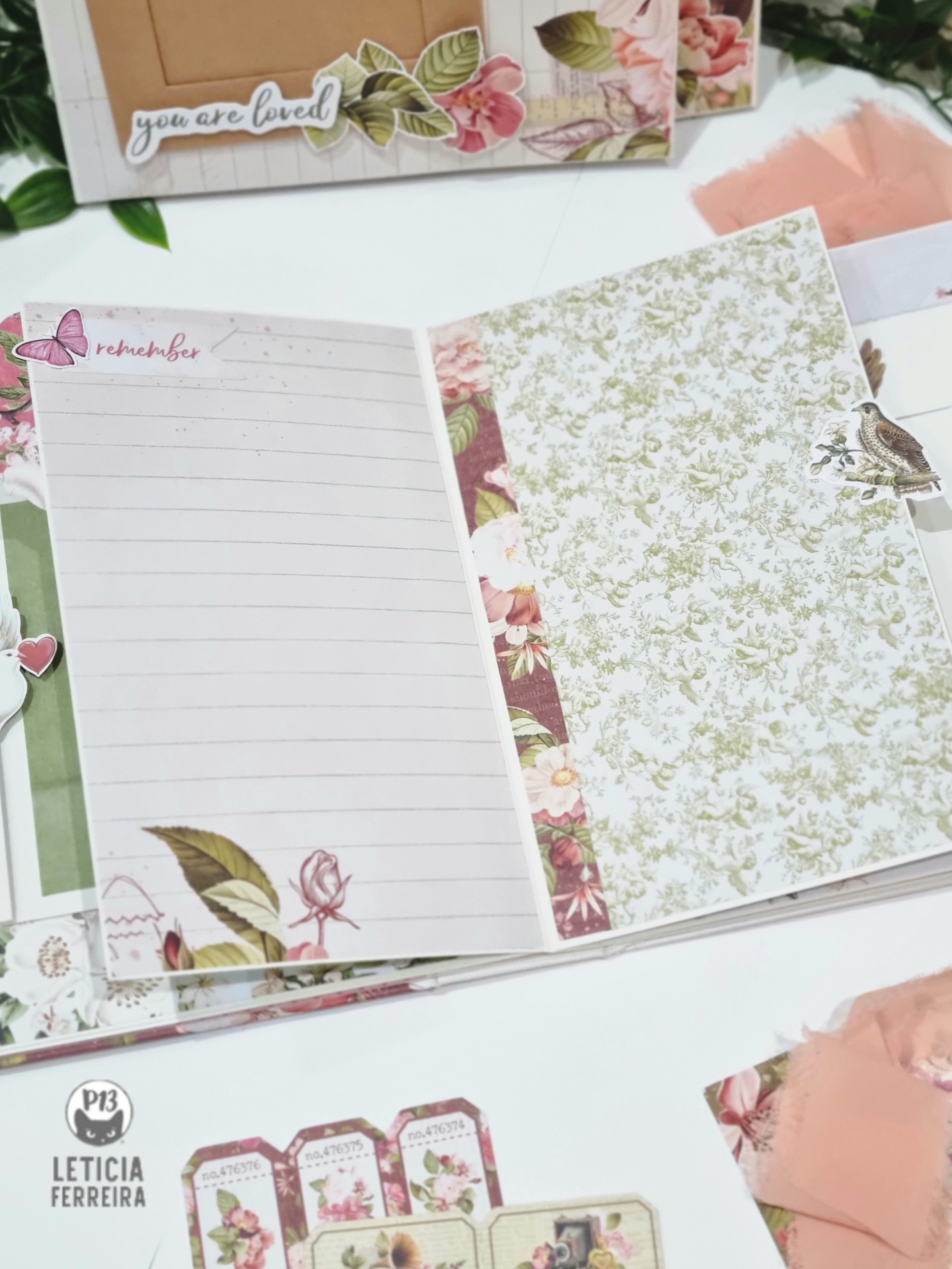 Caderno decorado com flores, folhas, texto 'remember' e cartão com 'you are loved'.