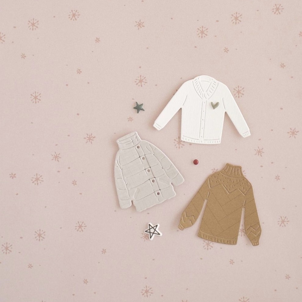 Três camisolas decorativas sobre fundo rosa com padrão de flocos de neve