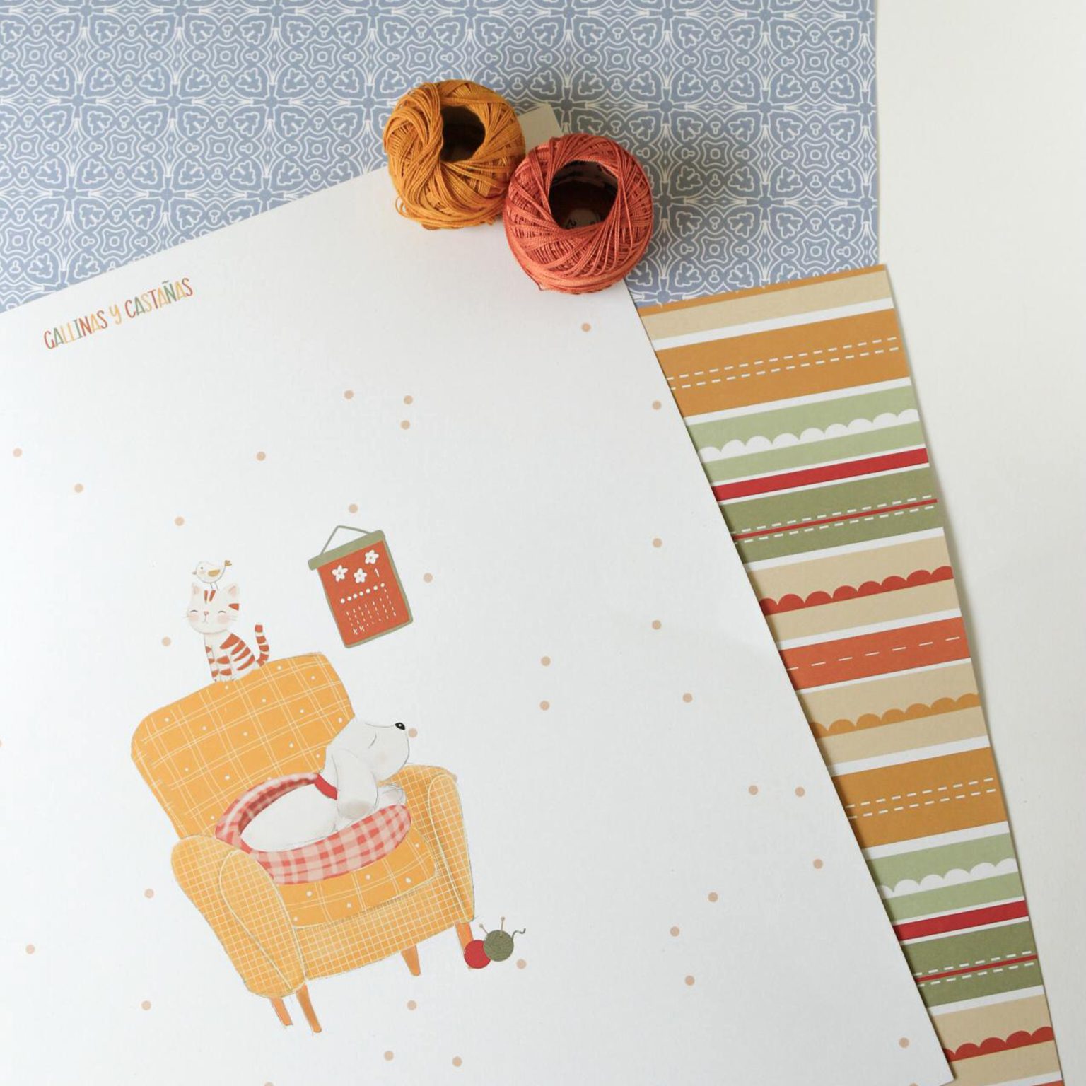 Papel decorativo com ilustração de cão, gato e pássaro numa cadeira amarela e dois novelos de lã coloridos.