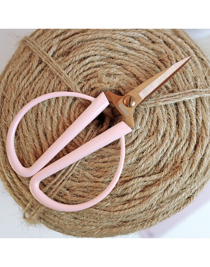 Tesoura pequena com cabos rosa claro sobre novelo de corda rústica