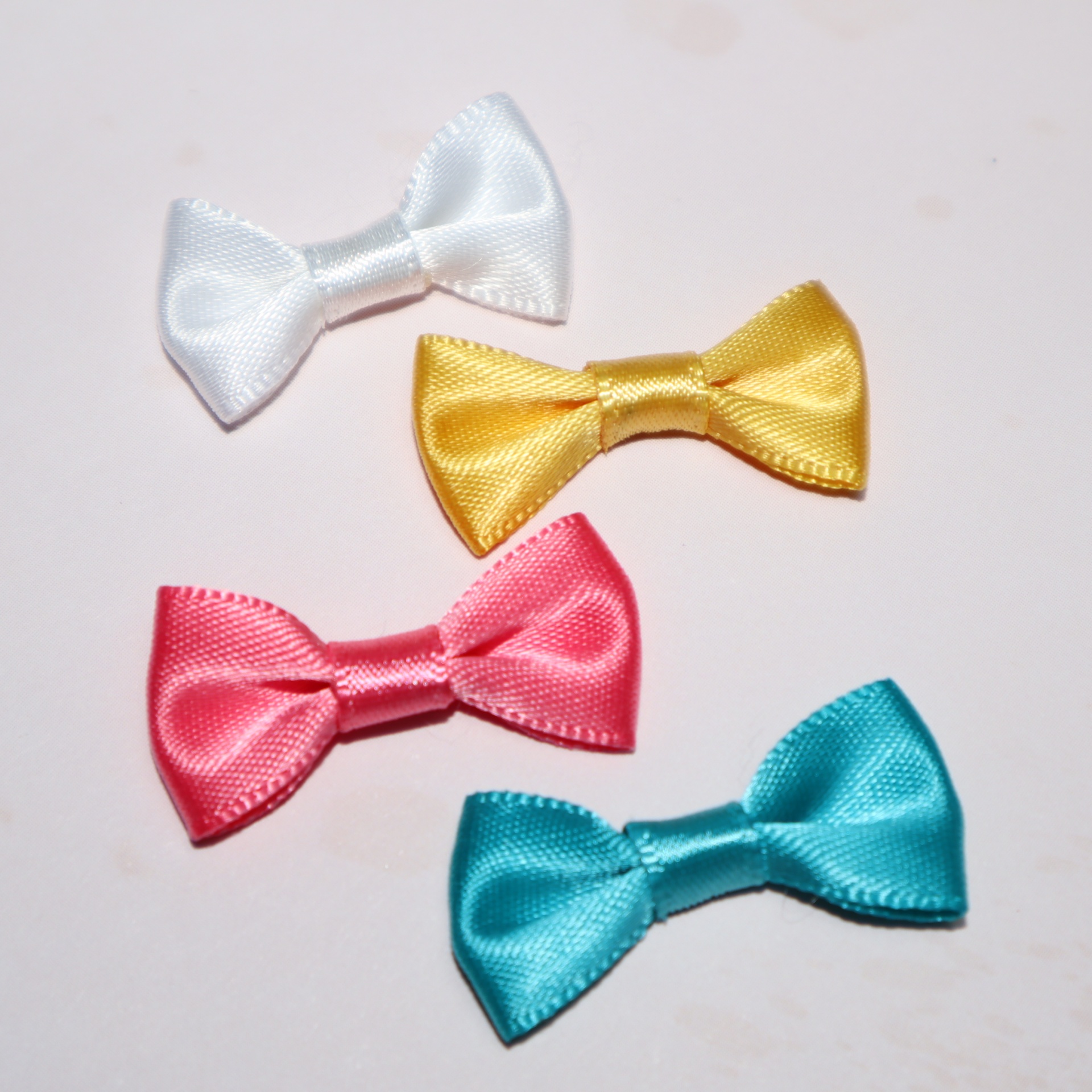 Quatro mini laços coloridos de cetim sobre fundo claro