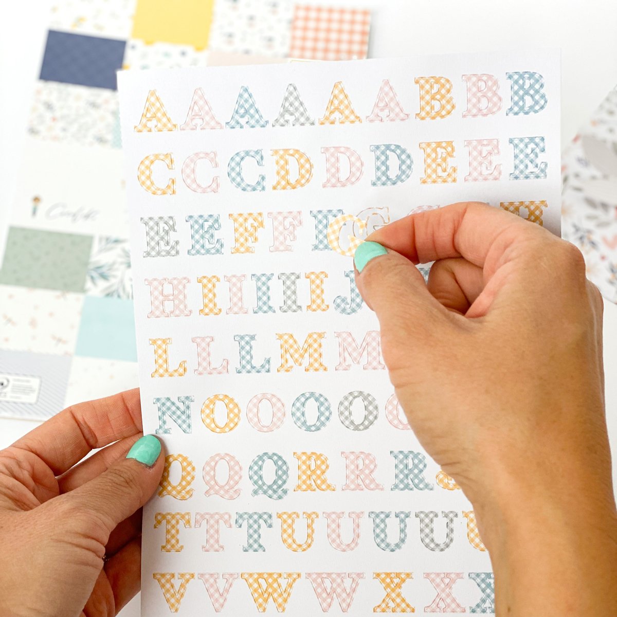 Folha com adesivos de letras coloridas sendo destacadas por mão feminina