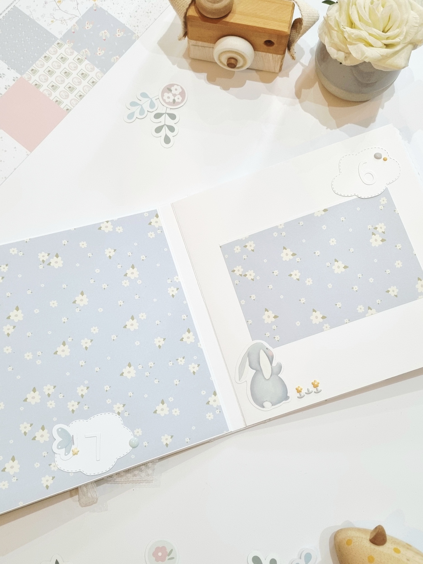 Livro bebé com padrão flores e ilustrações de coelho e números em nuvem, vaso com flor branca e bloco de madeira