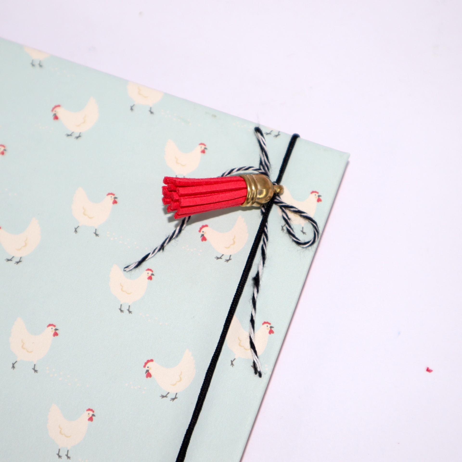 Caderno azul clara com padrão de galinhas e tassel vermelho com laço preto e branco