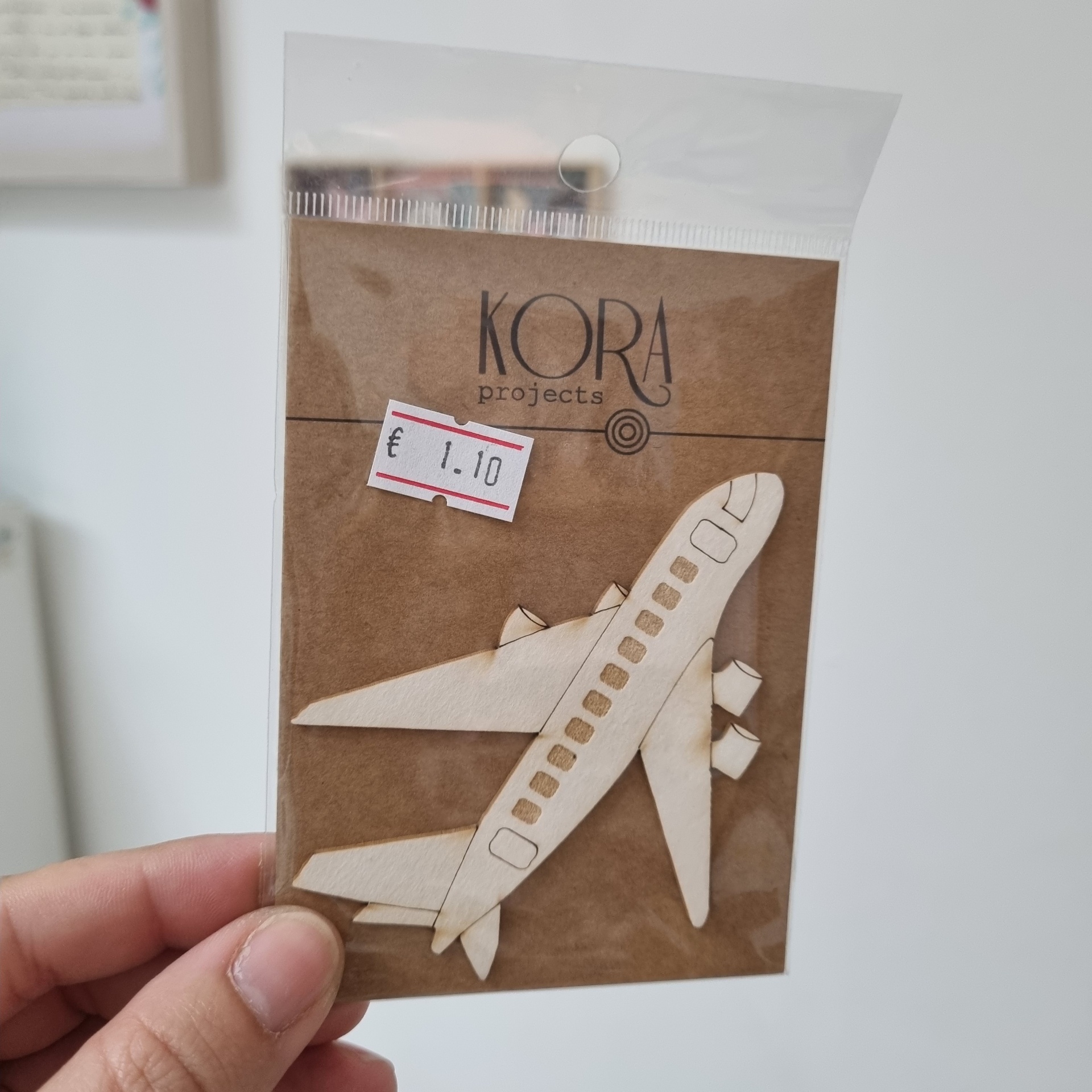 Modelo em madeira clara de avião embalado em plástico com cartão castanho com texto KORA projects