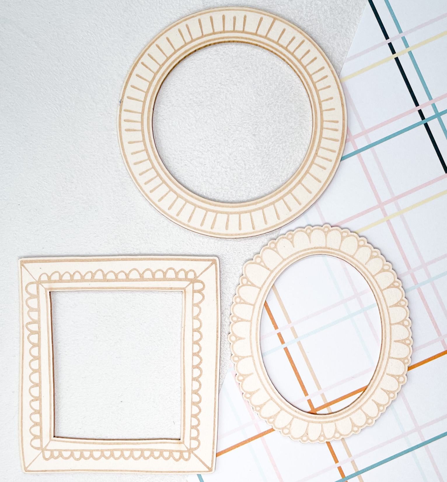 Três molduras decorativas de madeira clara com desenhos gravados em parede branca