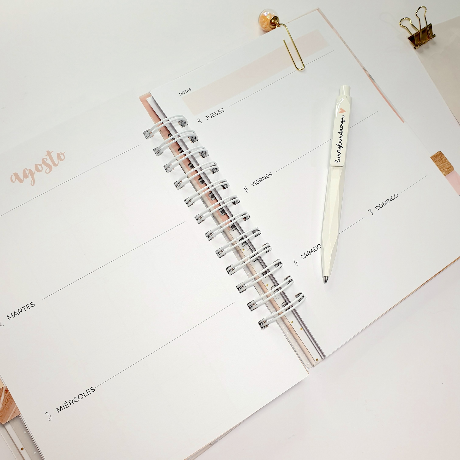 Agenda semanal aberta no mês de agosto com caneta branca e clips dourados