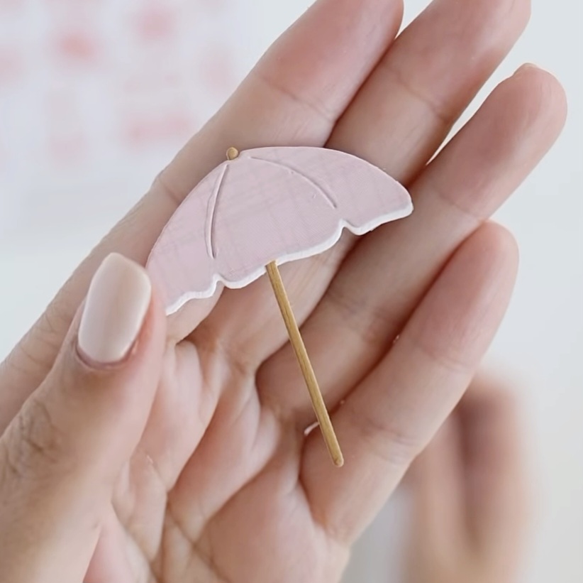 Miniatura de guarda-chuva rosa sendo segurada com unhas nude