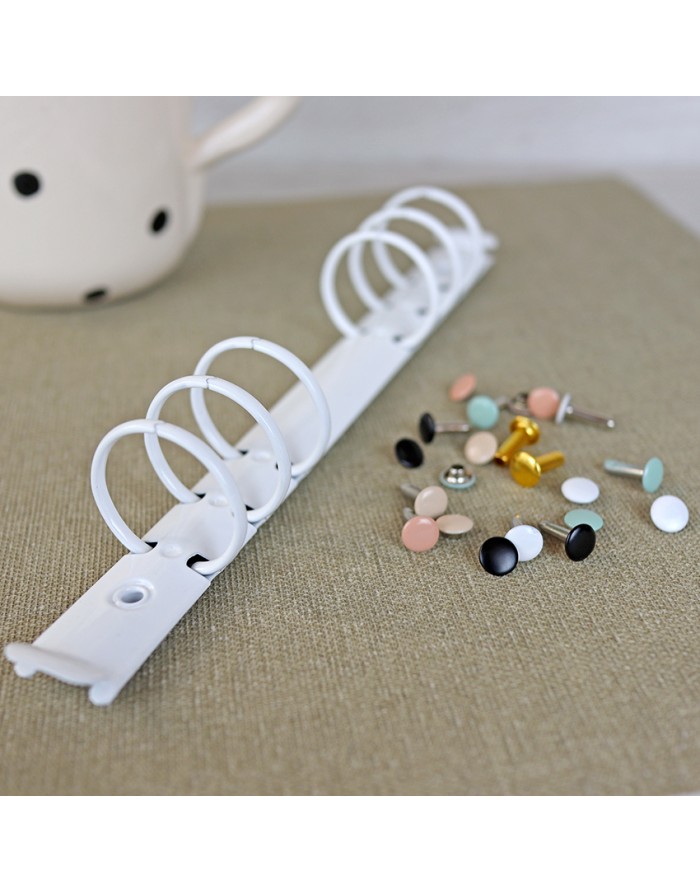 Argolas metálicas brancas para fichários junto a rebites coloridos sobre superfície castanha