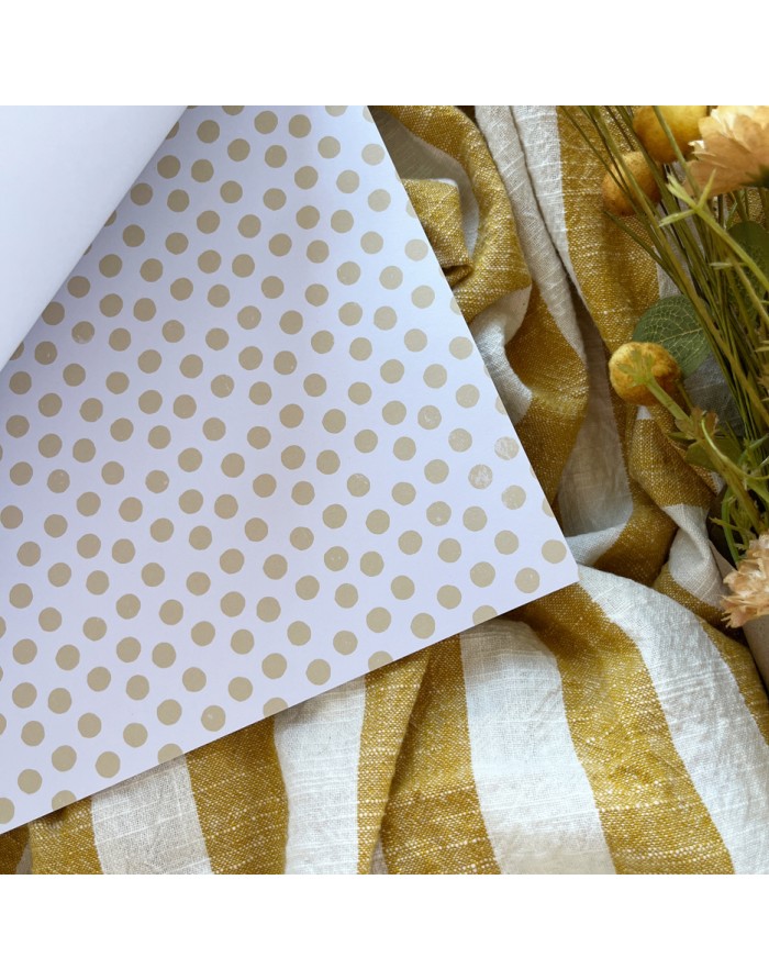 Papel de embrulho com padrão de bolinhas douradas sobre tecido riscado amarelo e branco com flores secas.