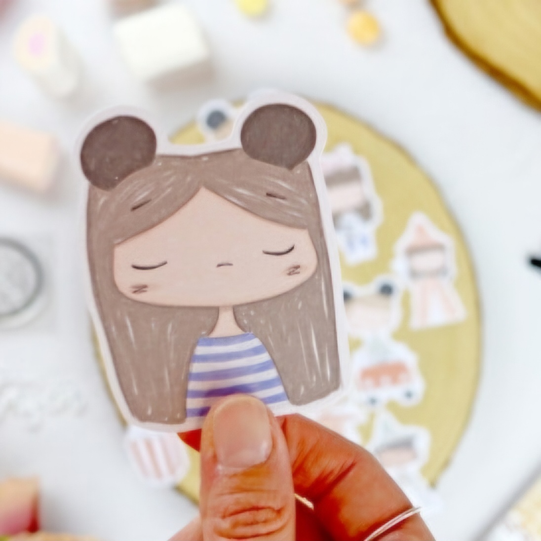 Autocolante de papel de personagem desenhada com orelhas de rato e roupa às riscas, mão a segurá-lo.