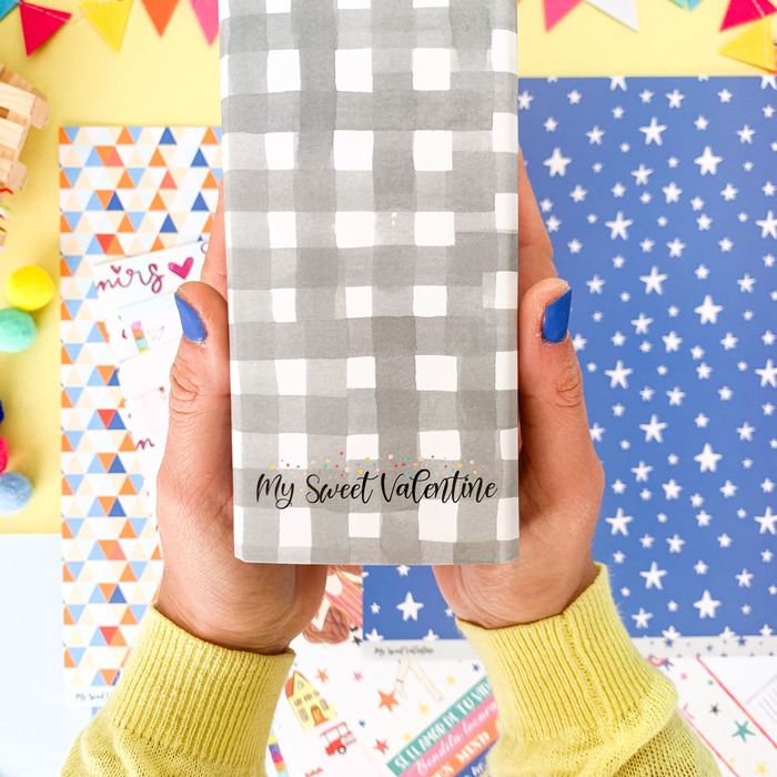 Pessoa segurando pacote cinza com padrão quadriculado e texto 'My Sweet Valentine'