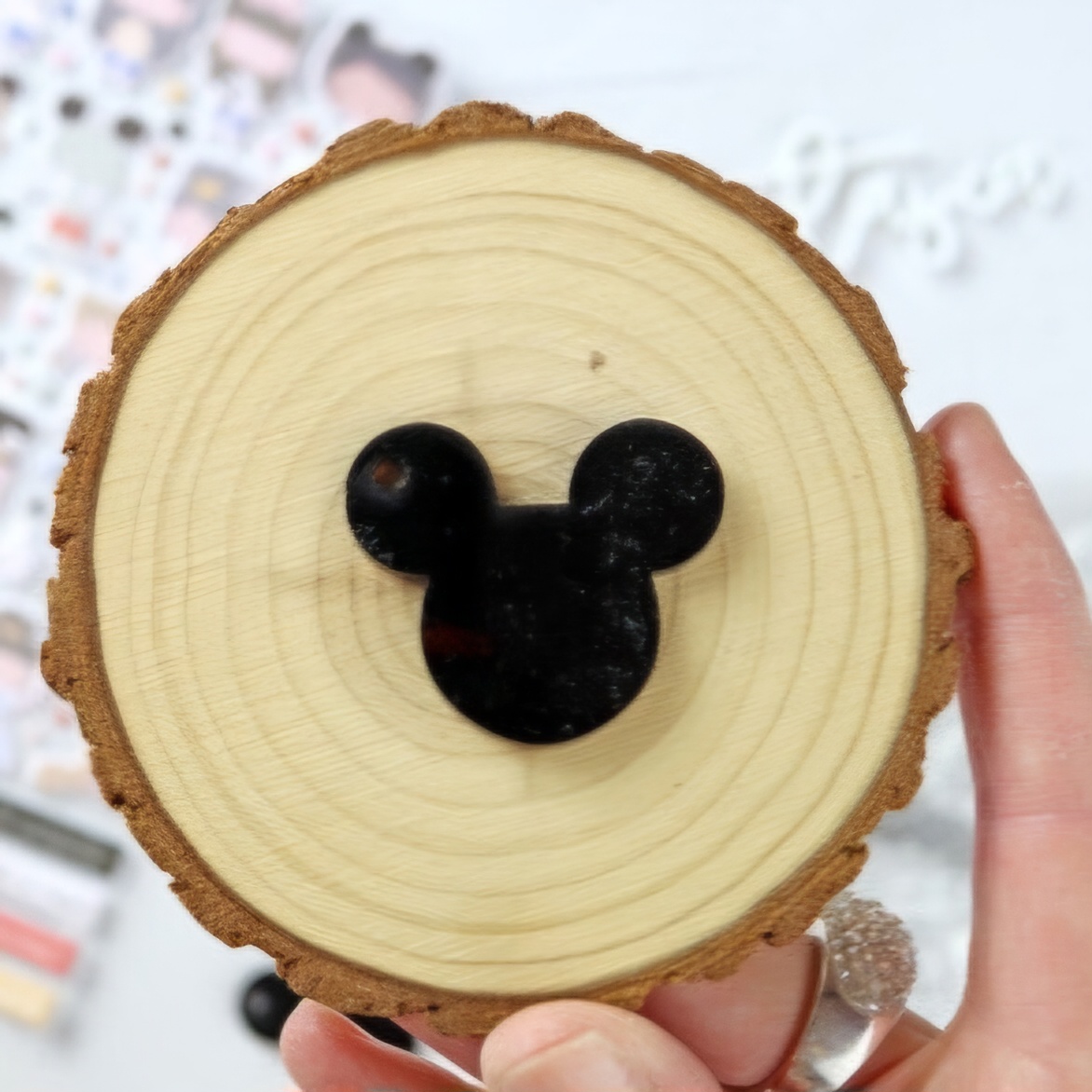 Objeto redondo de madeira com recorte preto em forma de cabeça de rato