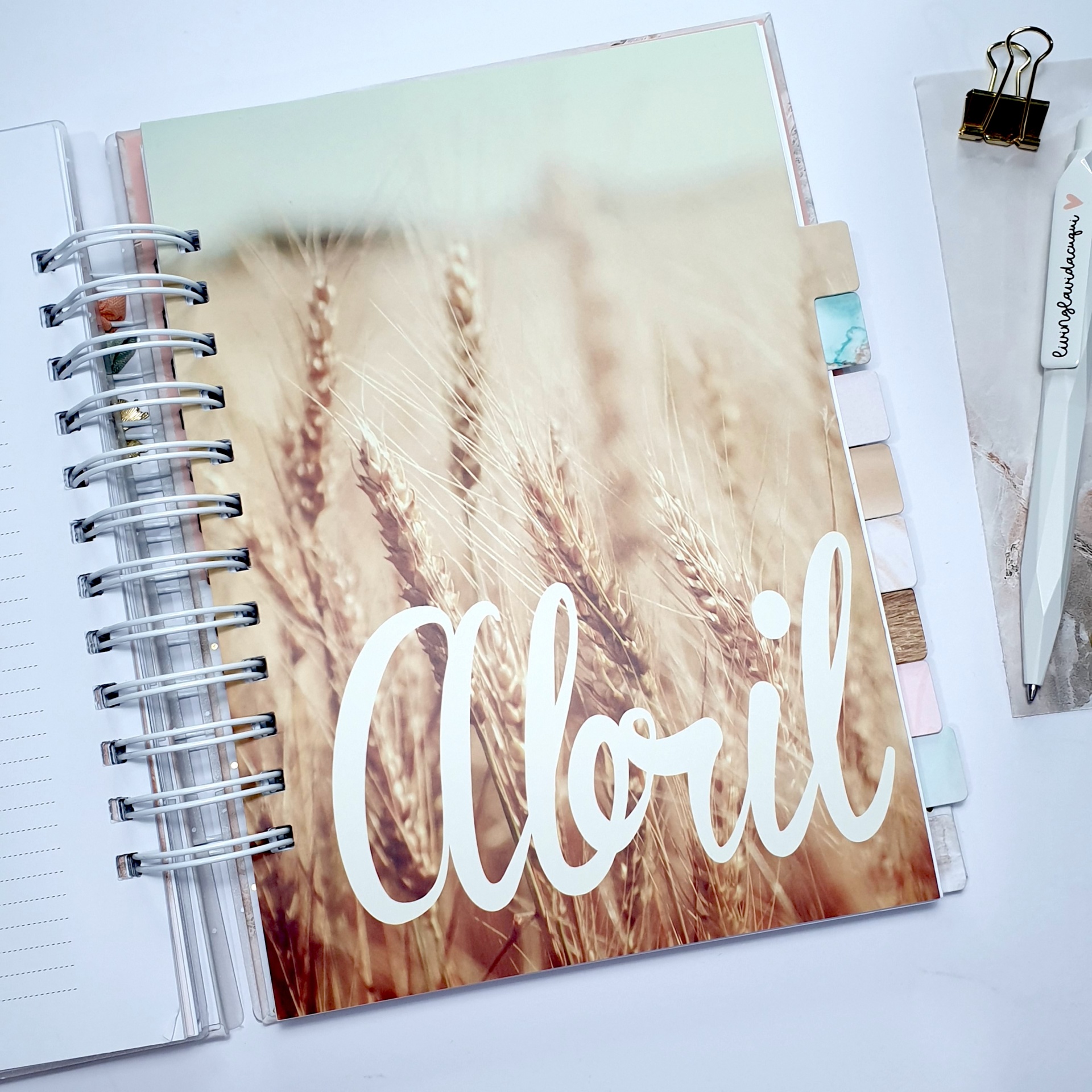 Planner aberto com capa do mês Abril com foto de trigo e texto branco cursivo