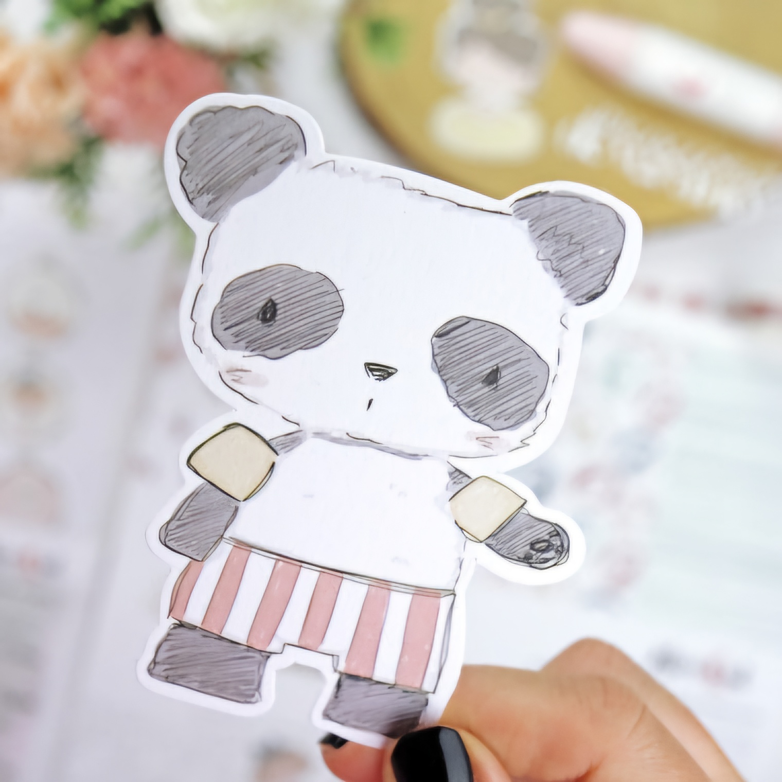 Autocolante decorativo de panda em tons cinzentos e branco com saia às riscas rosa e branco, segurado pela mão