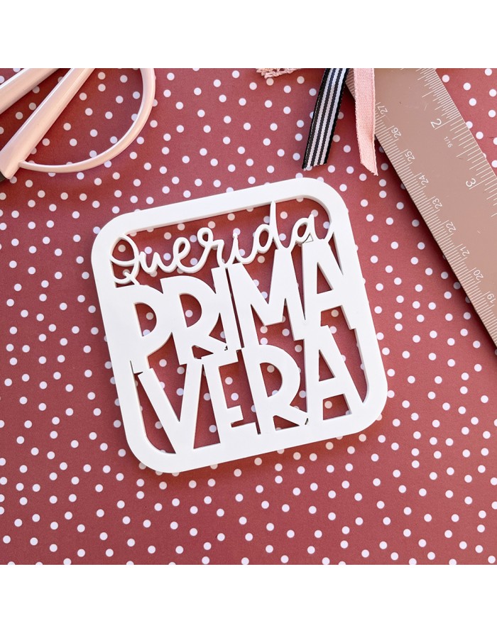 Etiqueta decorativa branca com texto 'Querida PRIMAVERA' sobre tecido castanho com bolinhas brancas