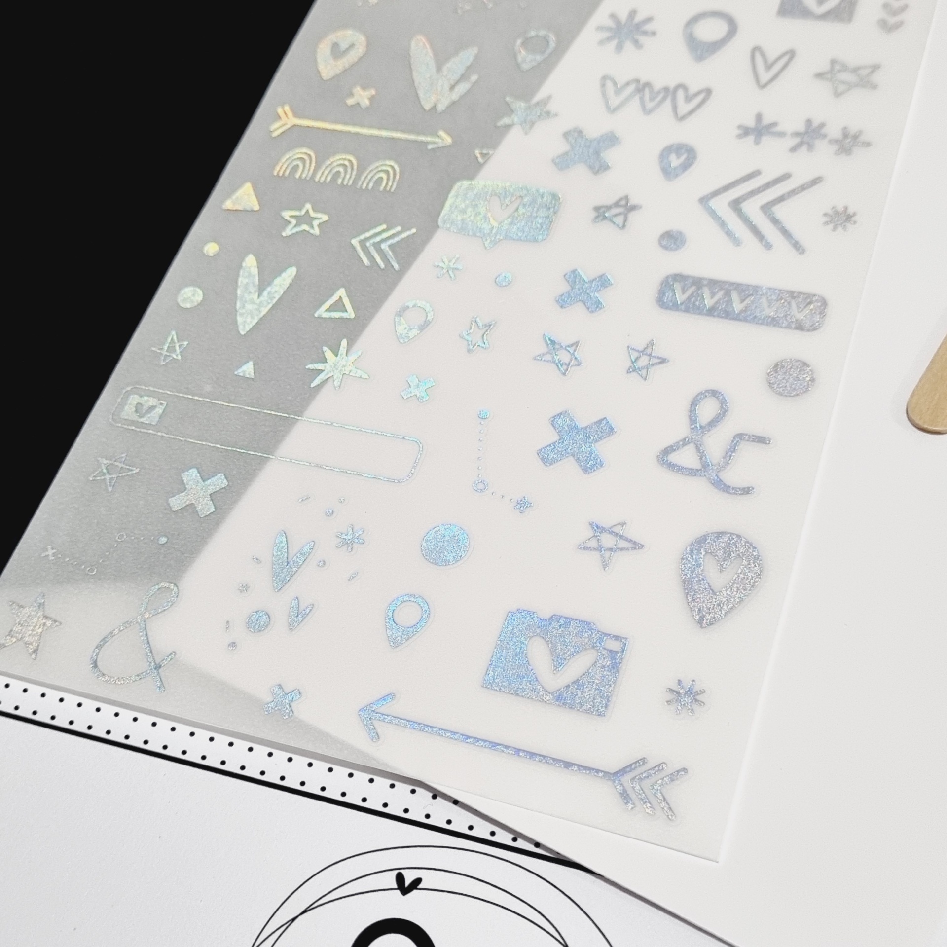 Folhas transparentes com autocolantes coloridos variados sobre mesa branca e preta