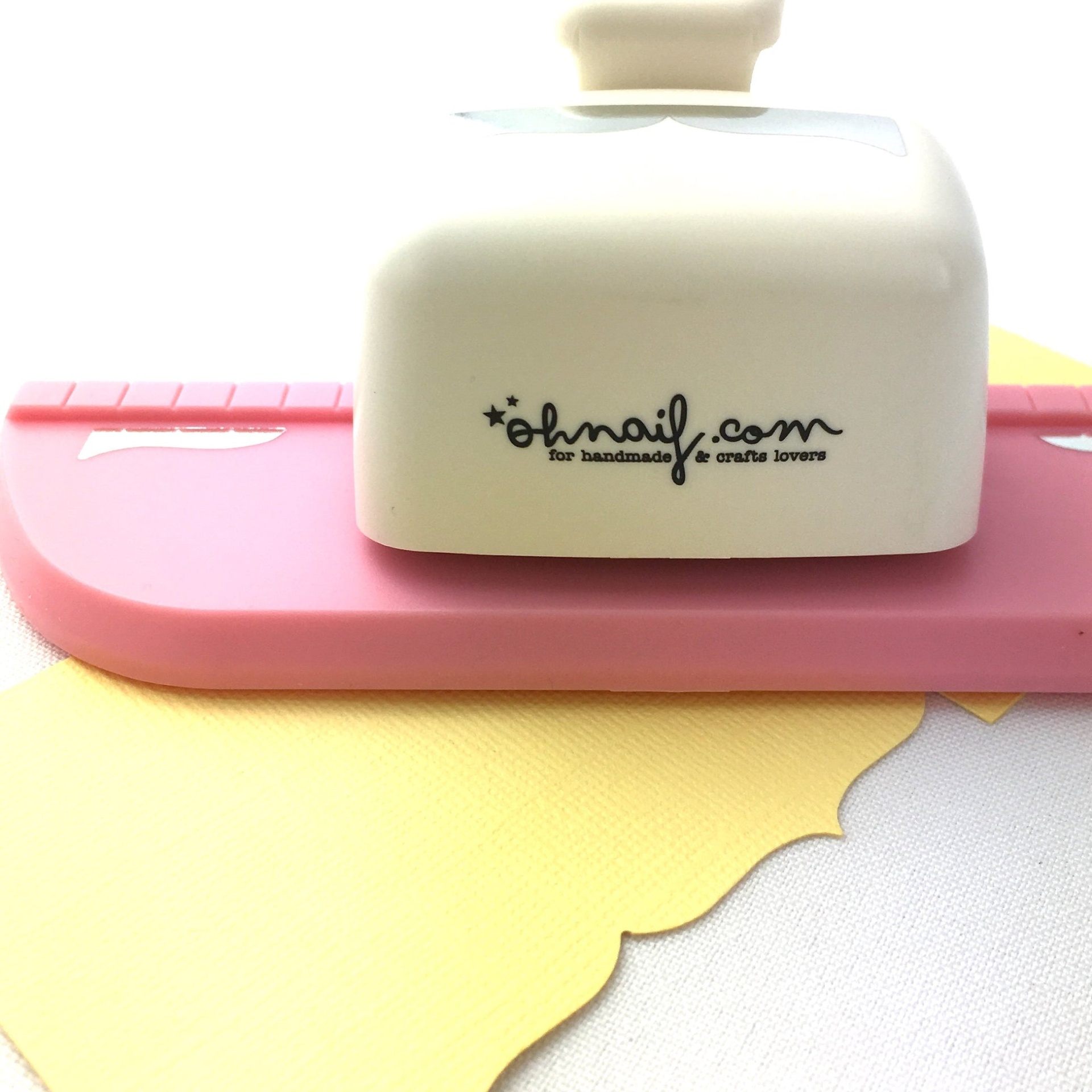 Dispositivo branco e rosa para cortar papel com logótipo ohnail.com sobre papel amarelo recortado