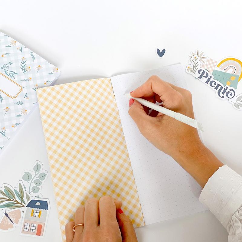 Pessoa escrevendo em caderno com capa xadrez amarelo e adesivos decorativos ao redor