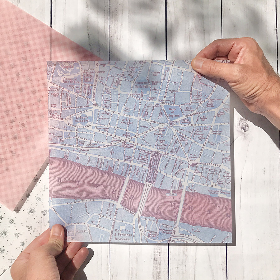 Mapa impresso a cores com ruas e rios, segurado por mãos, sobre madeira branca