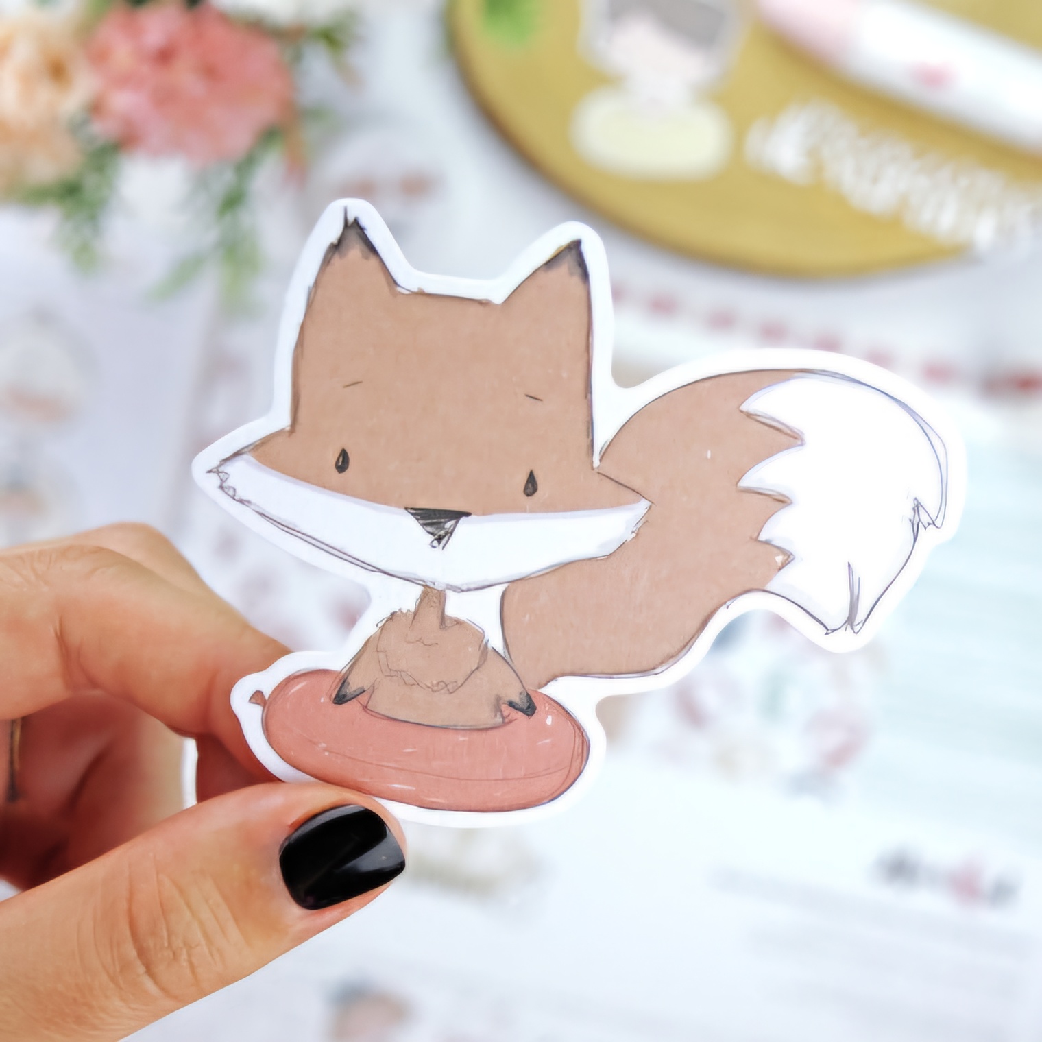 Adesivo de raposa castanha com detalhes brancos e olhos tristes segurado por mão com unhas pretas