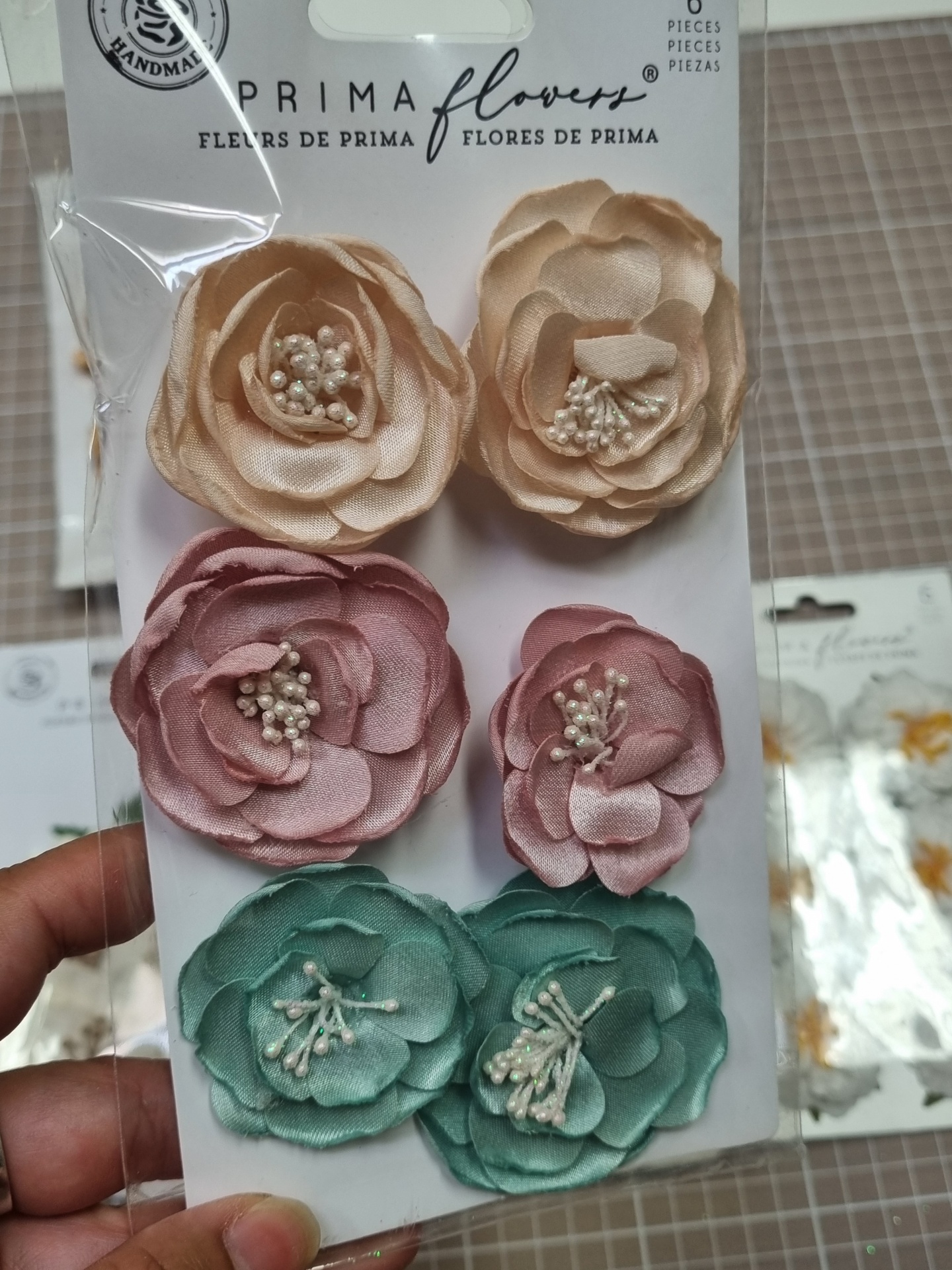 Flores artificiais em tecido bege, rosa e verde em embalagem da marca PRIMA flowers