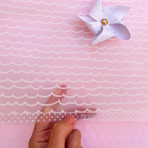 Régua transparente com bolinhas e coroa sobre fundo rosa claro com padrão de ondas e catavento lilás