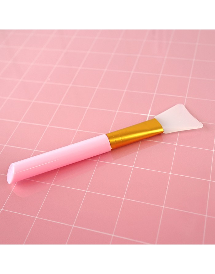 Pincel aplicador rosa com ponta de silicone transparente sobre superfície rosa quadriculada