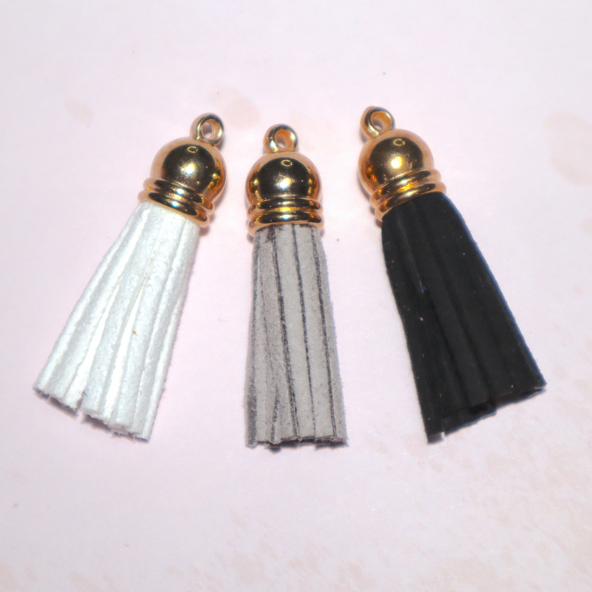 Três pompons de camurça em branco, cinzento e preto com topo dourado