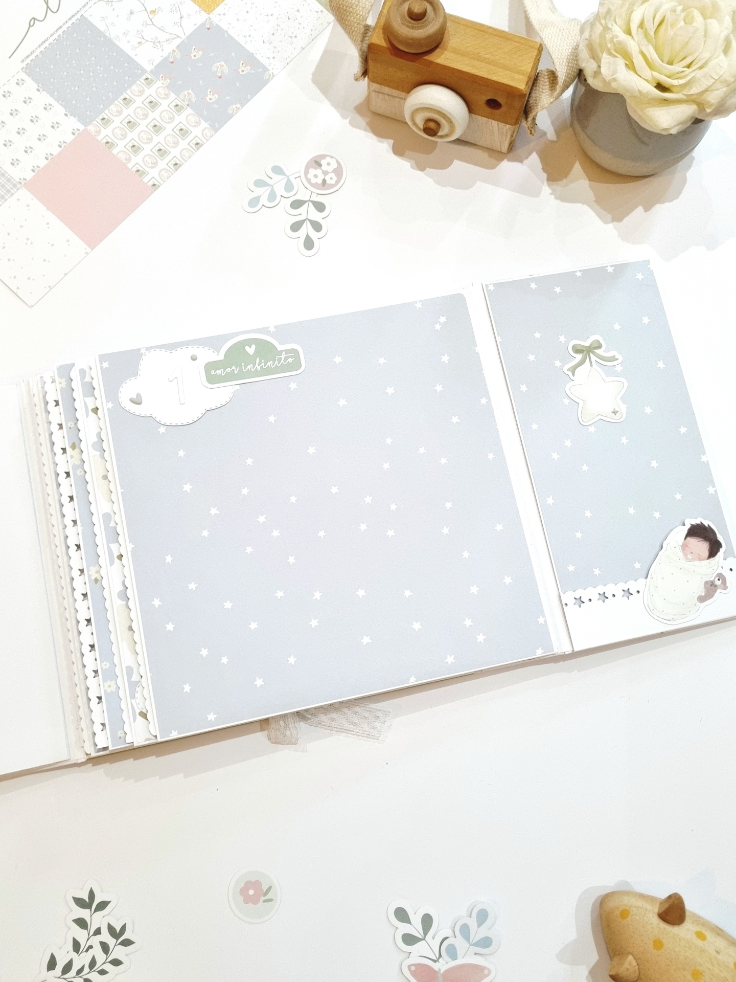 Livro de memória para bebés com páginas azuis estreladas, câmara de madeira e flor branca em vaso cinza