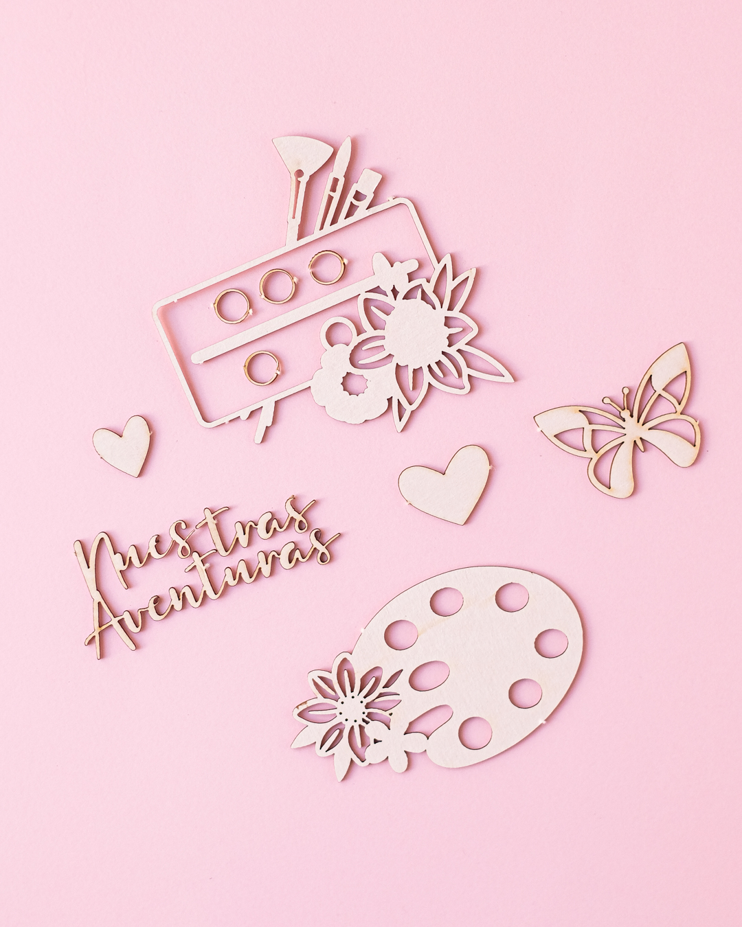 Elementos decorativos de madeira clara com tema artístico e floral sobre fundo rosa