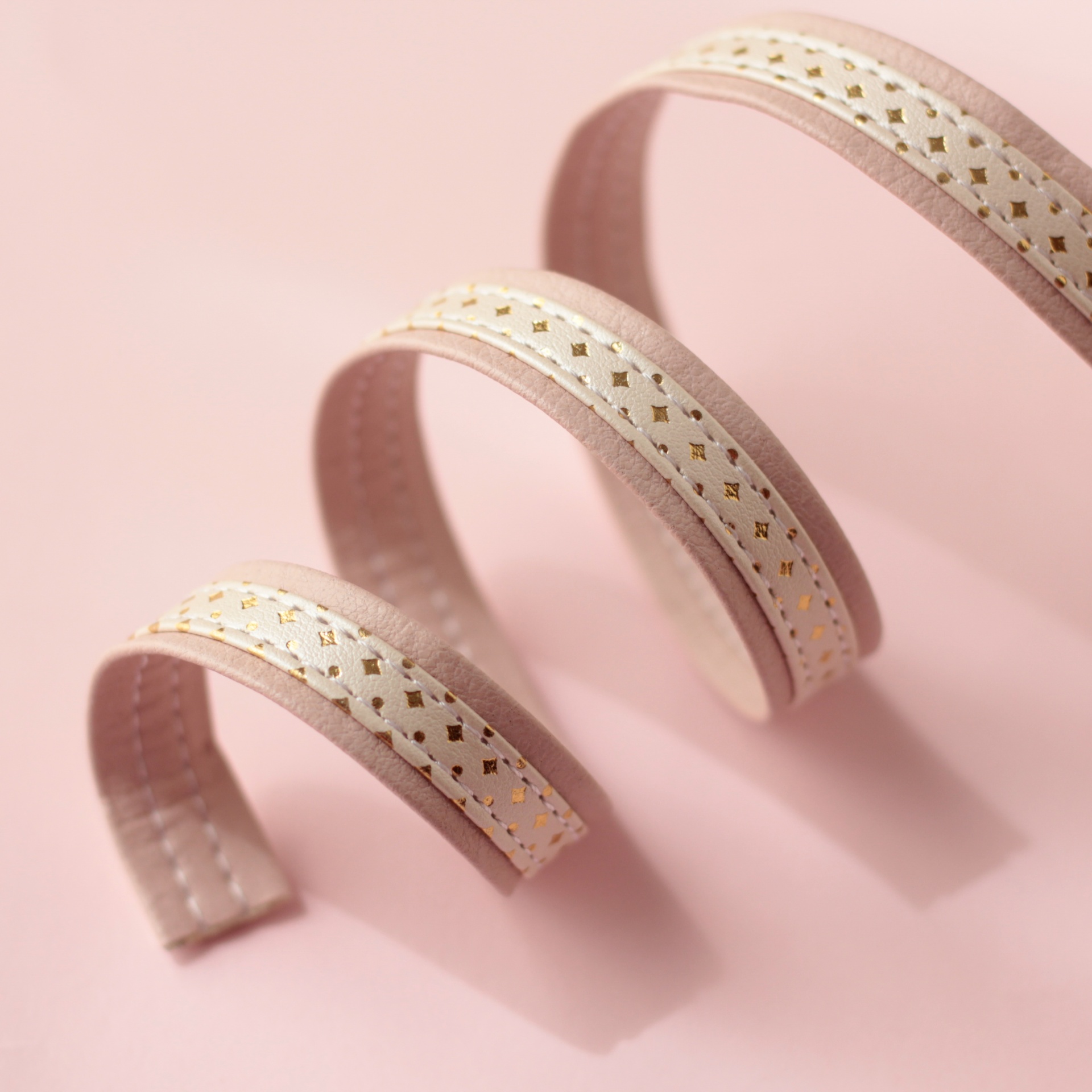 Três fitas decorativas enroladas em espiral sobre fundo rosa