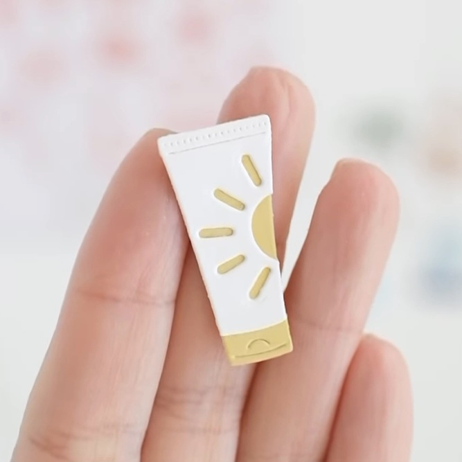 Miniatura de tubo de creme branco com sol amarelo, segurado entre dedos