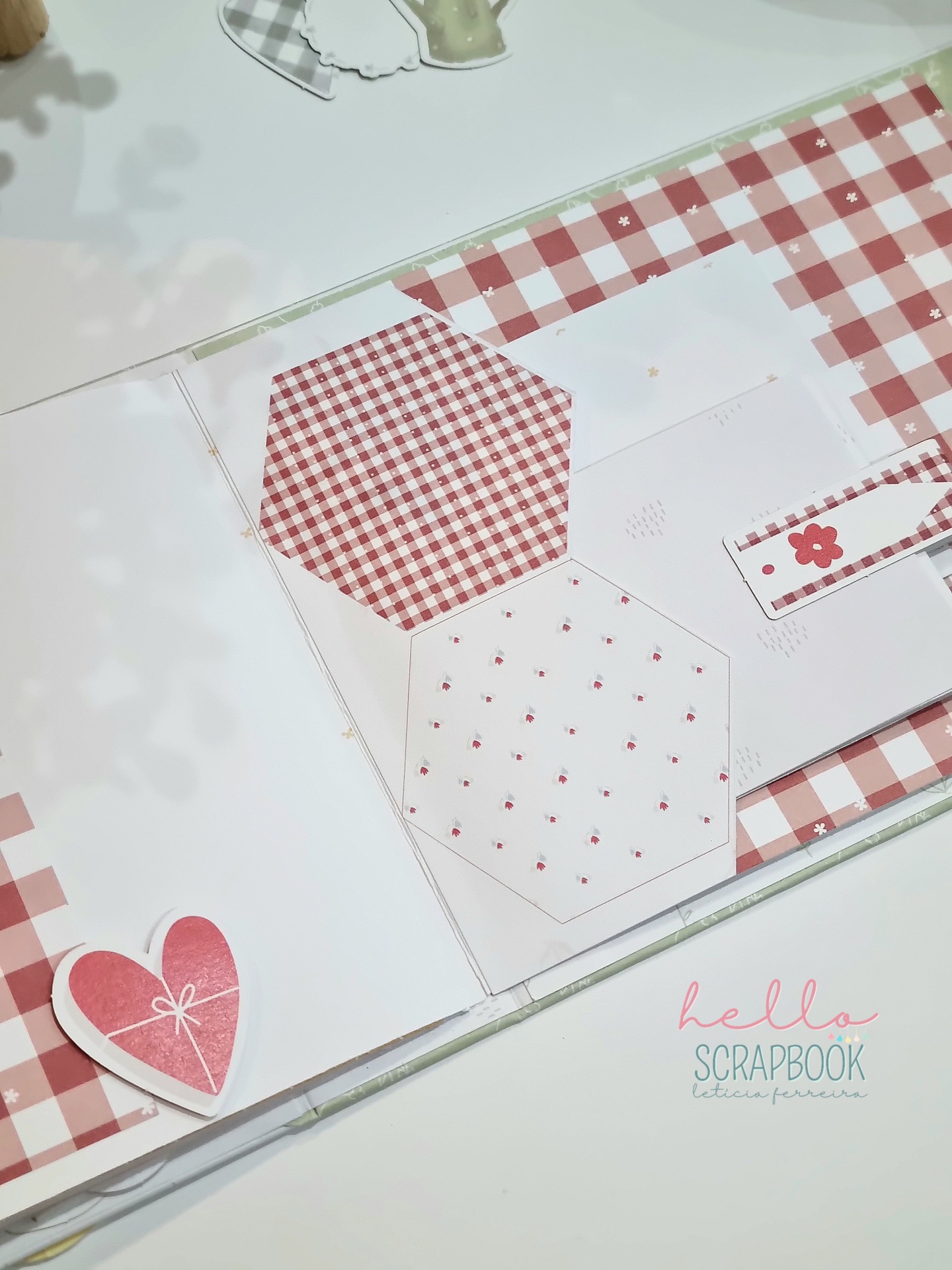 Livro de scrapbook com padrões vermelhos e decorações florais e de coração aberto num fundo claro