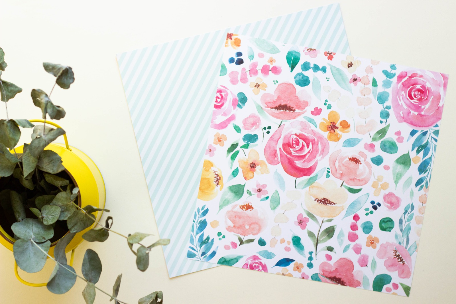 Lenços de tecido com padrões floral e de listras azuis ao lado de vaso amarelo com plantas.