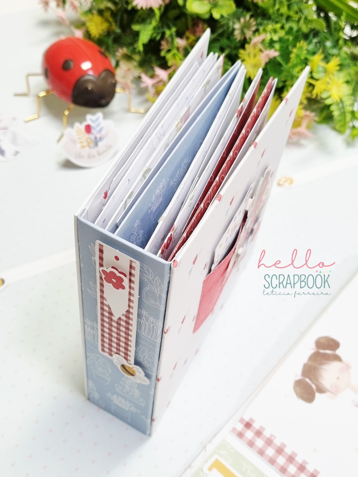 Álbum scrapbook decorado com padrões florais e xadrez ao lado de figura de joaninha