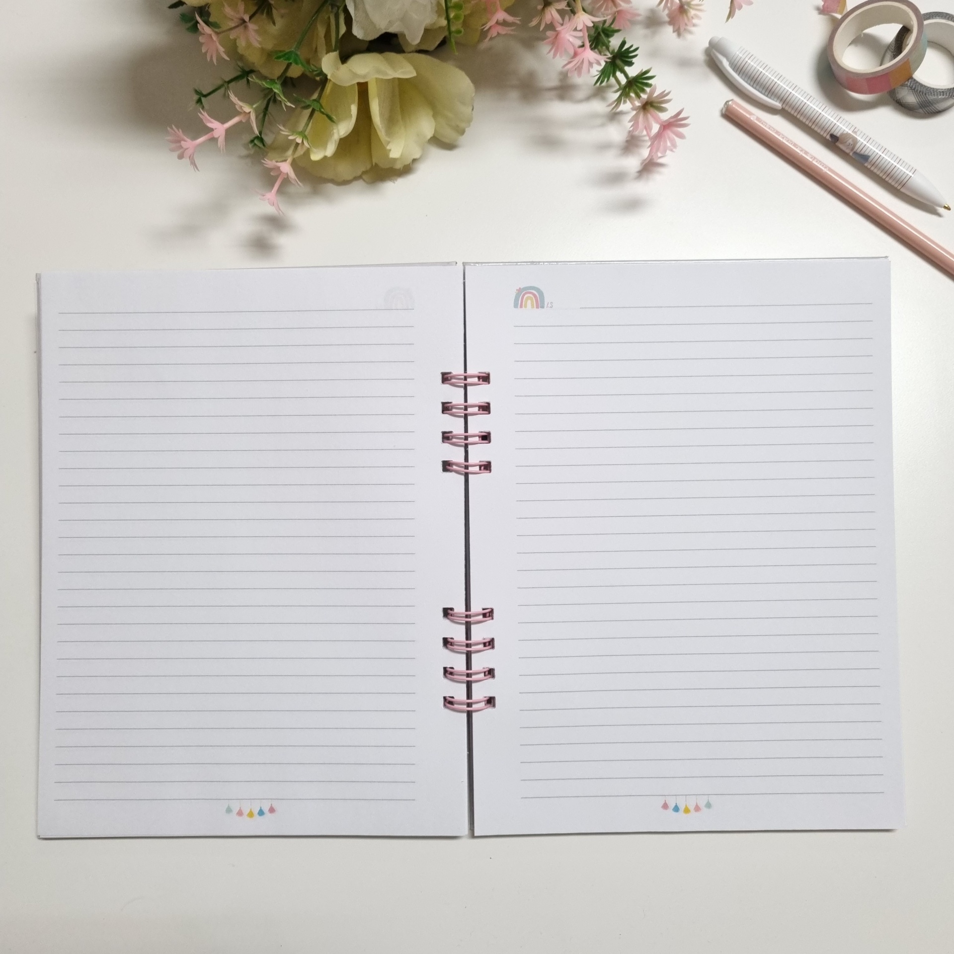 Caderno aberto com páginas pautadas e desenhos coloridos, flor artificial e acessórios de escritório sobre fundo branco