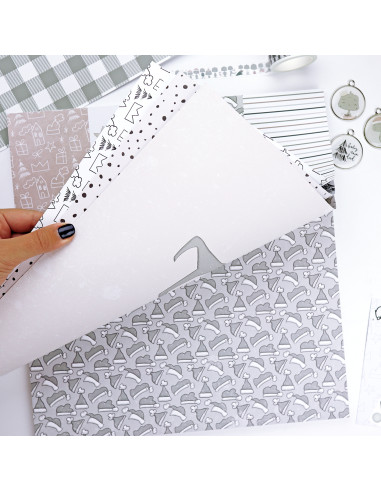 Folhas de papel decorativo com padrões natalícios e objetos de decoração em mesa branca