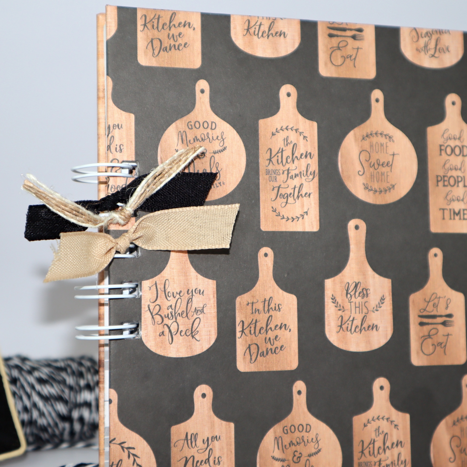 Caderno com capa preta decorada por tábuas de cozinha em madeira clara com texto em inglês e laços de tecido