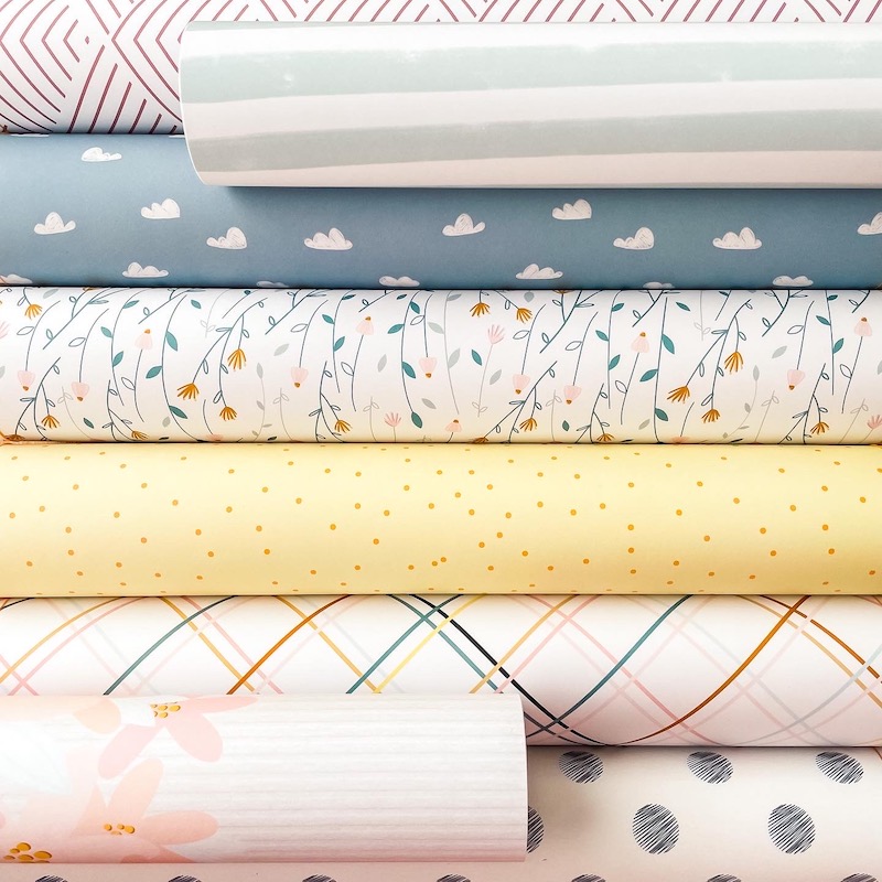 Tecidos enrolados com padrões geométricos, florais e de bolinhas em cores suaves, empilhados