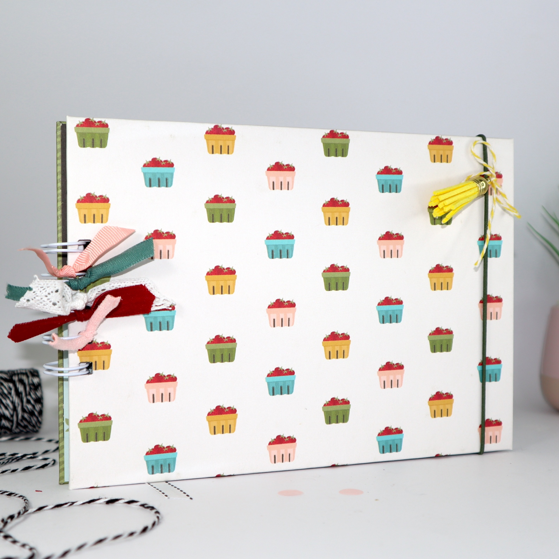 Caderno com capa branca decorada com pequenos cupcakes coloridos e fitas coloridas na encadernação