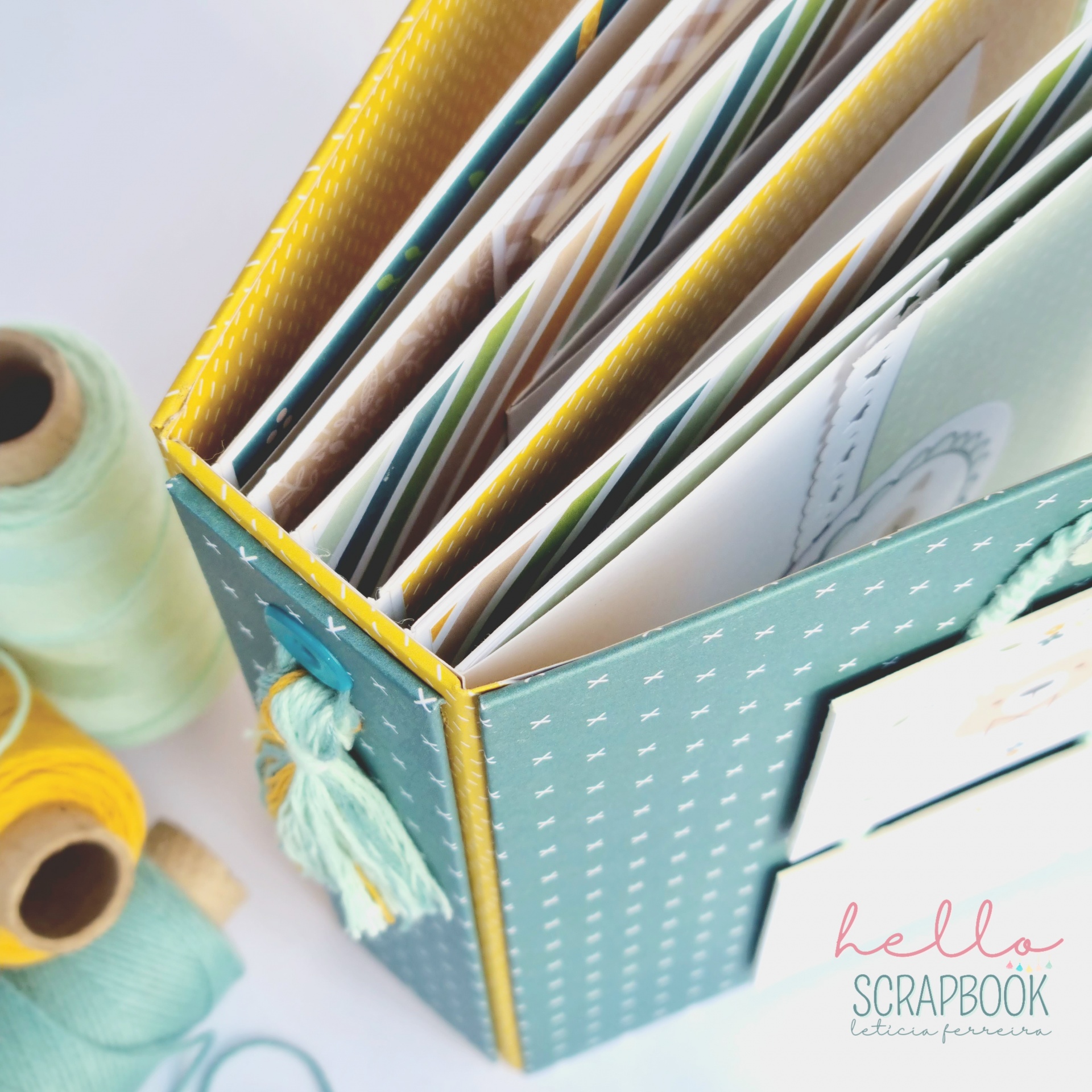 Álbum de scrapbook azul com padrão branco e tassel azul e amarelo numa mesa com rolos de fio