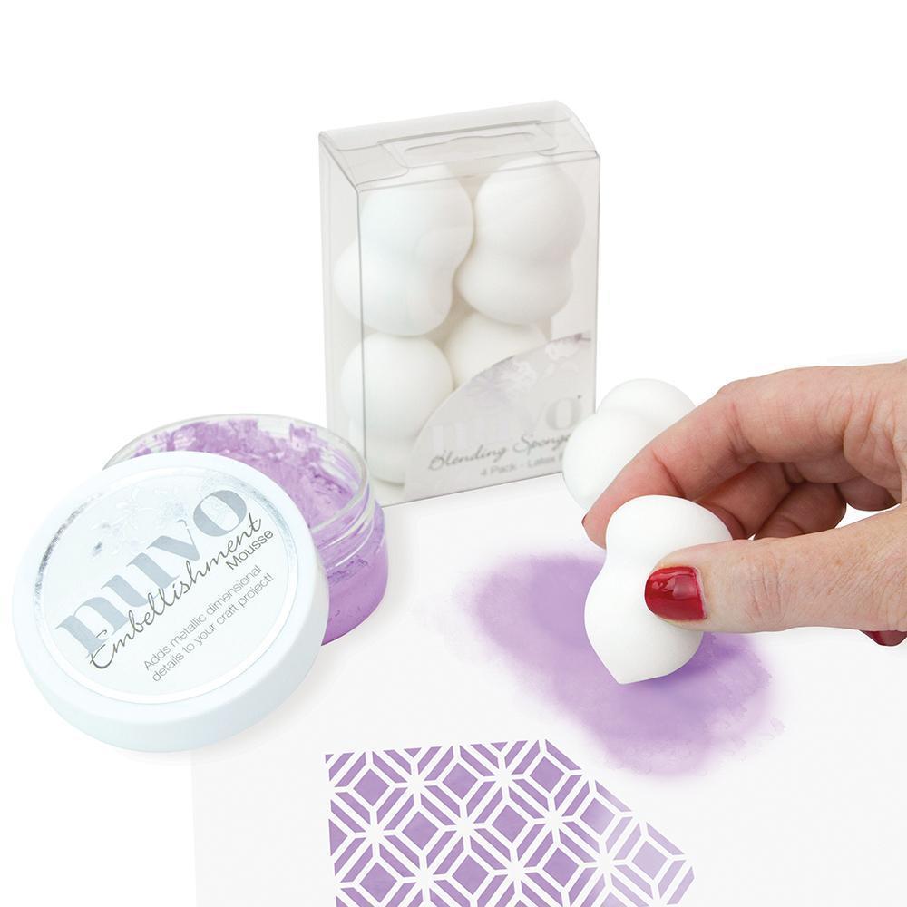 Mão aplicando pó roxo com esponja branca curva junto a recipiente e embalagem de esponjas.