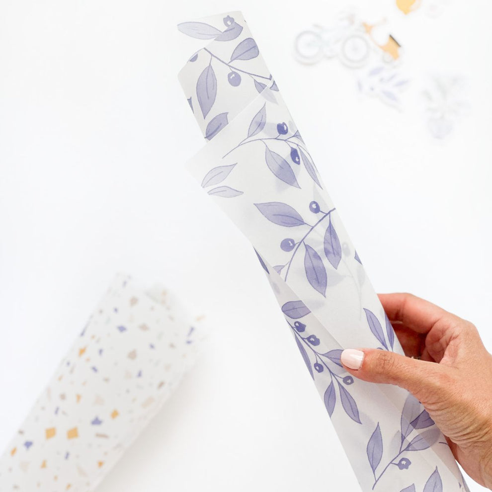 Rolo de papel decorativo com padrão de folhas cinza segurado por mão feminina