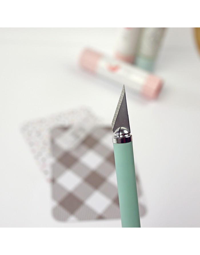 Faca de corte com lâmina triangular e cabo verde pastel em fundo com cartões e cola