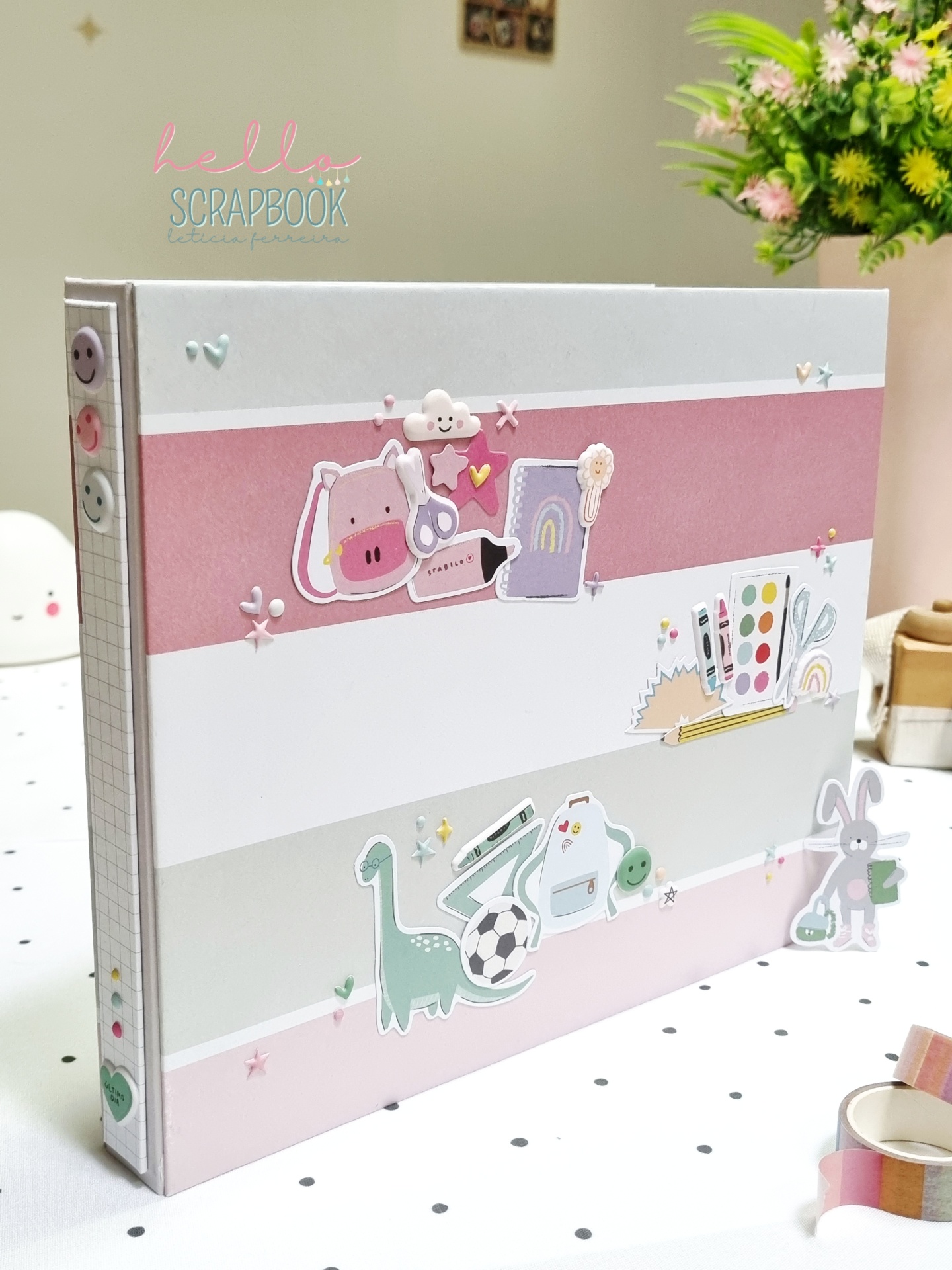 Álbum scrapbook com faixas coloridas e adesivos decorativos sobre mesa com toalha pontilhada