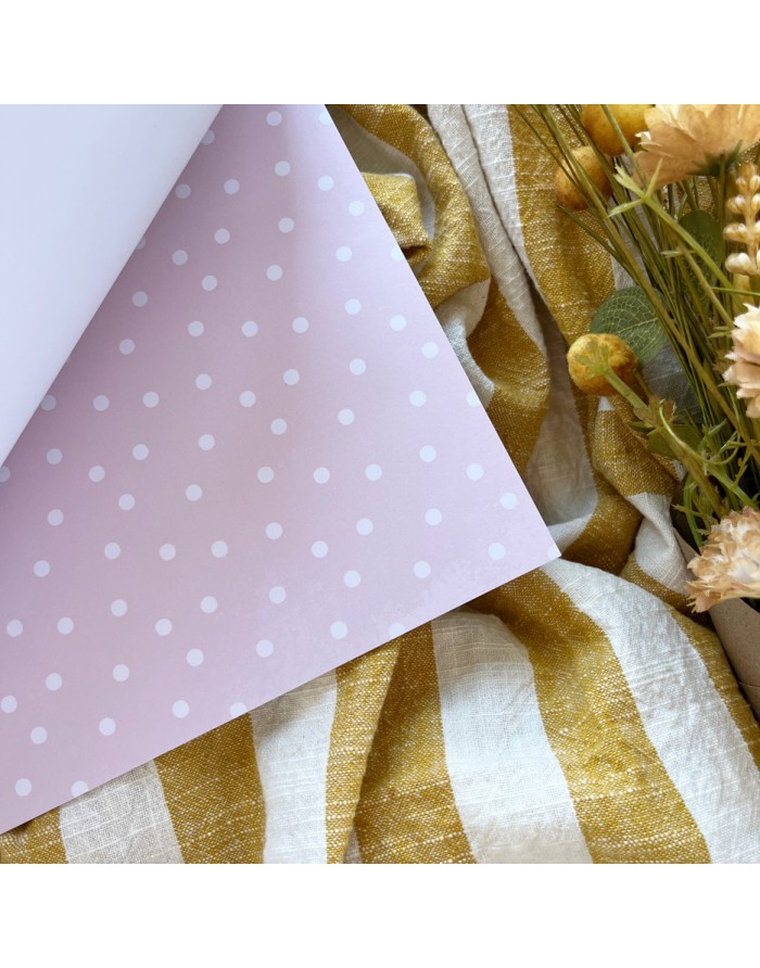 Papel rosa com bolinhas brancas sobre tecido com riscas amarelo-mostarda e branco junto a flores secas