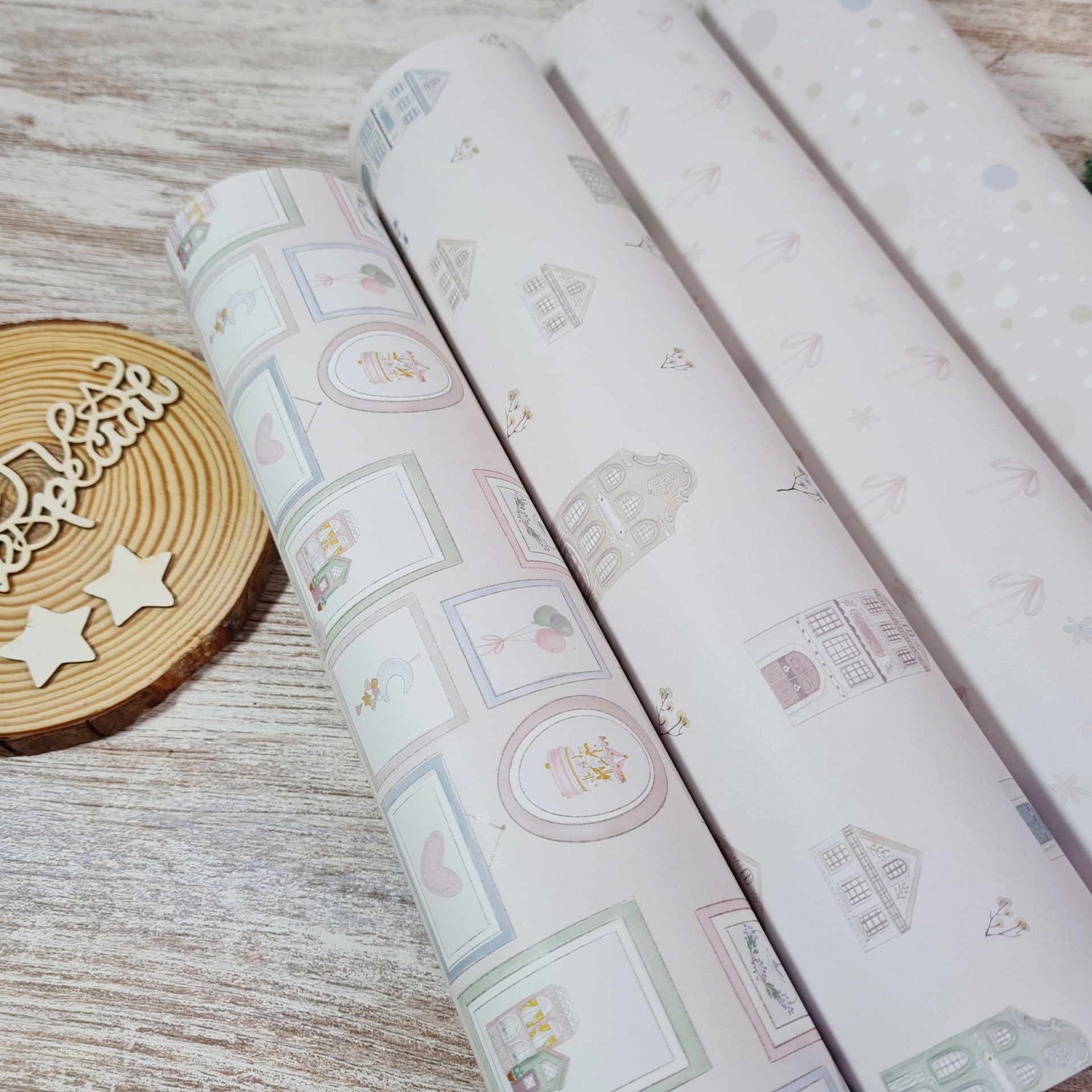 Quatro rolos de papel de embrulho com padrões pastel e suporte de madeira com estrelas