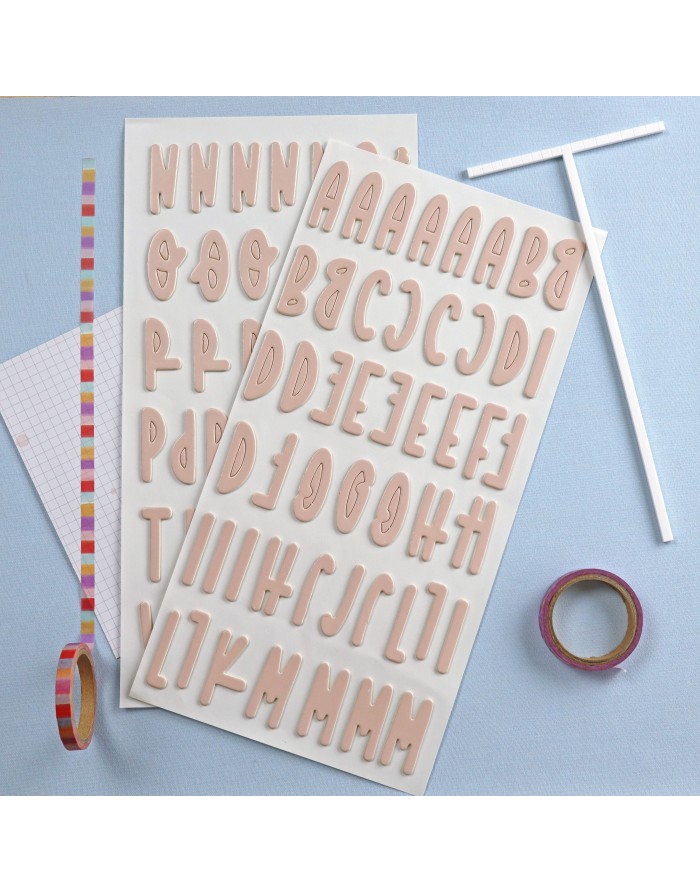 Autocolantes de letras maiúsculas bege em folhas com fita adesiva colorida e papel quadriculado